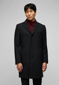 Dunkelgrauer Wollmantel mit taillierter Passform, einreihigem Design, Reverskragen und Brusttasche. Auffällige schwarze Knöpfe heben die Details hervor.