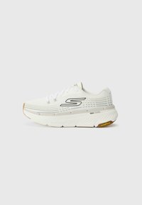 Zapato deportivo blanco con parte superior de malla texturizada, acentos negros, suela gruesa acolchada y suela de goma de color goma. Presenta cordones y detalles del logo.
