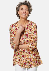 Blumige Tunika-Bluse in Gelb mit roten und grünen Mustern, rundem Ausschnitt und Dreiviertelärmeln. Weicher, leichter Stoff.