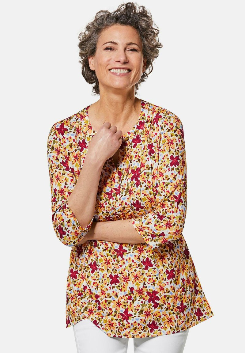 Blumige Tunika-Bluse in Gelb mit roten und grünen Mustern, rundem Ausschnitt und Dreiviertelärmeln. Weicher, leichter Stoff.