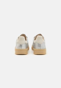 Sølvmetalliske joggesko med beige elementer, en teksturert finish og en polstret såle; har logo på hælen og bølgede detaljer.