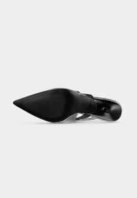 Chaussure noire à talon haut à bout pointu vue de la semelle, montrant un talon stiletto fin et une semelle texturée.