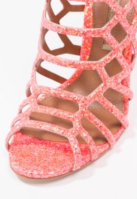 Glittrig rosa sandalett med öppen skärdesign, smala remmar och en texturerad plattform. Har en slät innersula och en stabil klack.