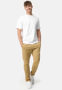 Camiseta blanca de manga corta, chinos caqui y zapatillas blancas. Look casual con un diseño simple y textura de tela ligera.