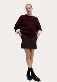 Bordeaux oversized wolblend trui met een ronde hals, gecombineerd met een bruine leren minirok. Zwarte sokken en gepolijste loafers ronden de look af.