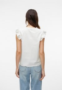 Witte blouse met gerimpelde schoudermouwen, een zachte textuur en een ronde halslijn, gecombineerd met lichtblauwe high-waisted denim jeans.