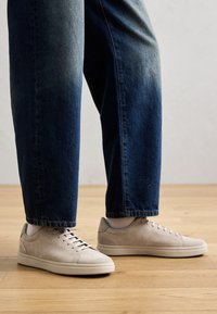 Baskets en daim beige à texture lisse, semelles en caoutchouc blanc et six œillets, associées à un jean denim bleu foncé fuselé.