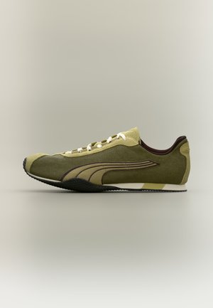 Lavprofileret olivengrøn sneaker med beige og brun Puma-logo, hvide snørebånd, tekstureret sål og en blød hælkant.