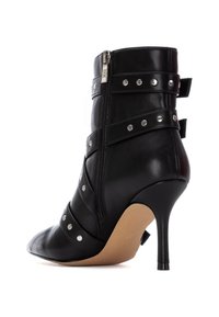 Bota de tobillo de cuero negro con punta afilada, tacón alto, cierre de cremallera y múltiples correas decorativas con tachuelas metálicas.