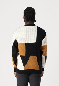 Sweter dzianinowy z geometrycznymi blokami kolorów w czerni, kremie i musztardzie, ozdobiony wzorami warkoczy, z prążkowanymi mankietami i okrągłym dekoltem.