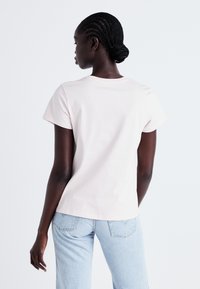 T-shirt rose clair à manches courtes avec un col rond, associé à un jean en denim bleu clair, montrant une vue de dos et une texture de tissu lisse.