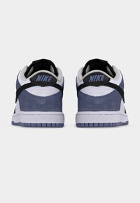 Ζευγάρι χαμηλά αθλητικά παπούτσια Nike σε λευκό, ναυτικό μπλε και μαύρο, φωτογραφημένα από πίσω, εμφανίζοντας το λογότυπο της Nike στις ταμπελίτσες της φτέρνας σε απλό φόντο.