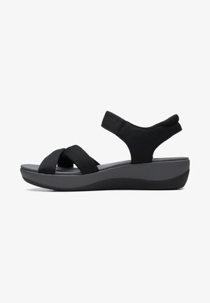 Sandales noires avec des bretelles élastiques croisées et une semelle grise rembourrée. Elles disposent d'un talon compensé et d'une lanière de cheville rembourrée pour un meilleur maintien.