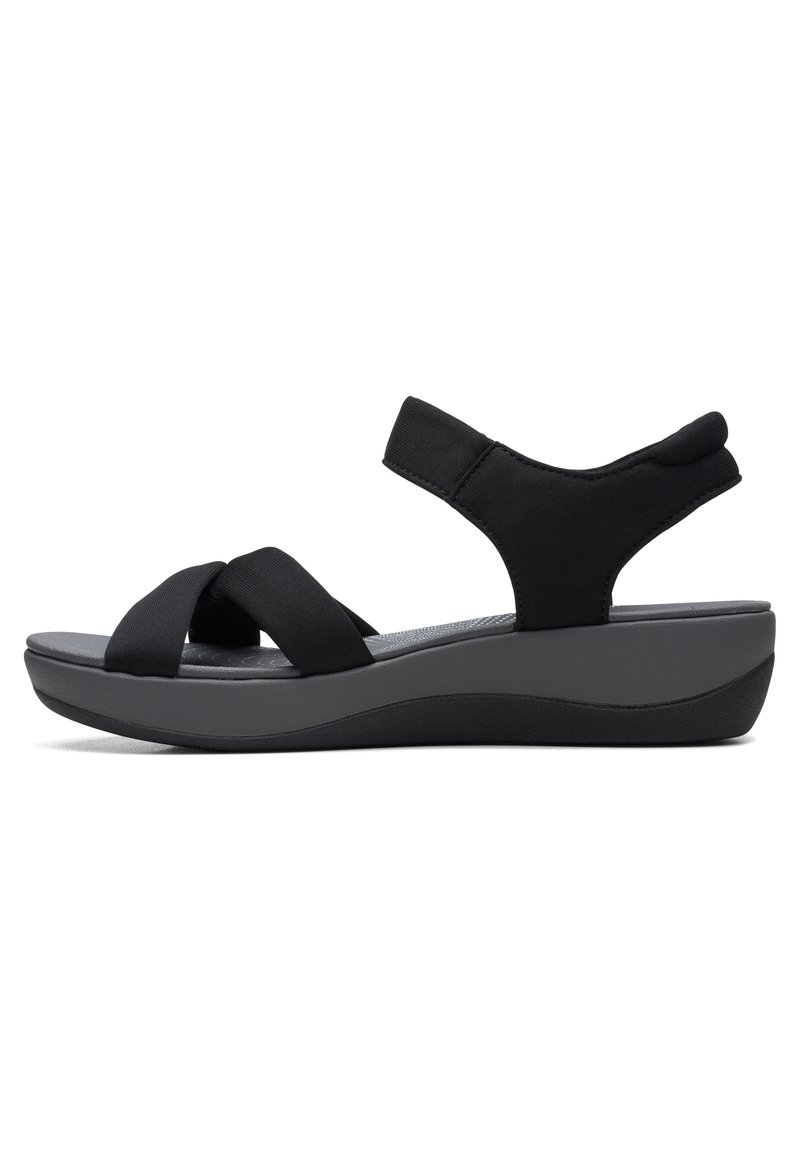 Schwarze Sandalen mit überkreuzten elastischen Riemen und einer gepolsterten grauen Sohle. Sie verfügen über einen Wedge-Absatz und einen gepolsterten Knöchelriemen für Unterstützung.