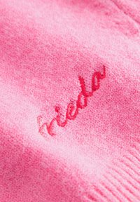 Roze gebreide stof met een zachte textuur, voorzien van een rode geborduurde tekstdetail. Het ontwerp is eenvoudig en uniform van kleur.