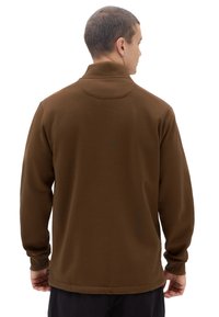 Pullover marrone a maniche lunghe con colletto alto, texture liscia e polsini a coste. La parte posteriore presenta un dettaglio a yoke rotondo e un'etichetta discreta.