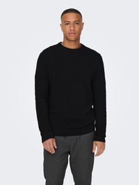 Black knit sweater with a textured pattern, round neckline, and ribbed cuffs and hem. Worn with gray pinstriped trousers.