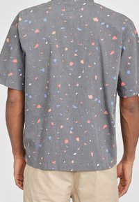 Camicetta a maniche corte in tessuto grigio con un motivo a macchie nei toni corallo, blu e bianco. Design casual con una vestibilità comoda.