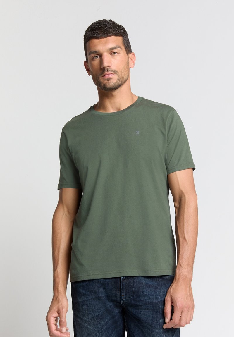 Olijfgroen katoenen T-shirt met een ronde hals en korte mouwen, met een klein logo-detail op de borst. Draagt men met blauwe denim jeans.