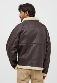 Giacca di pelle marrone con colletto e polsini in shearling, caratterizzata da una vestibilità boxy e dettagli di cucitura visibili.
