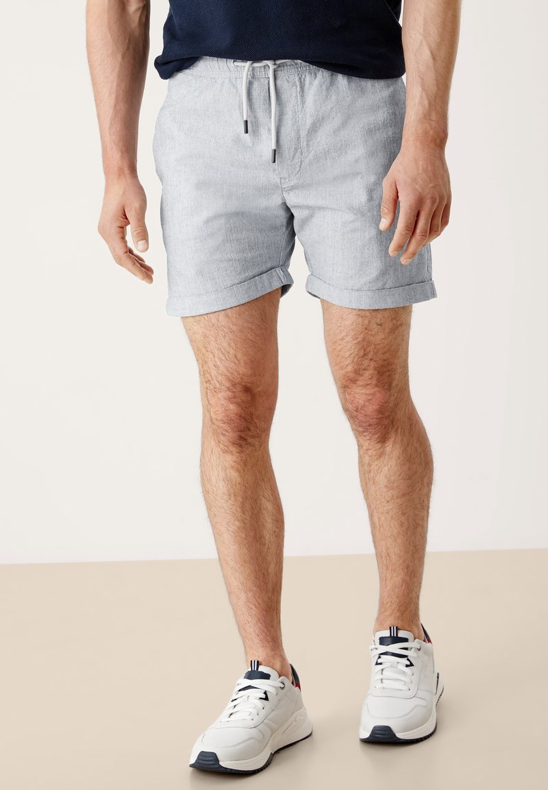 Shorts gris clair à l'apparence texturée, dotés d'une taille à cordon de serrage et d'ourlets retroussés, assortis à des baskets blanches avec des accents bleu marine.