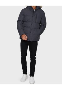 Mørkegrå dunjakke med pelsforet hætte, frontlomme med lynlås og knaplukninger. Sat sammen med sorte bukser og hvide sneakers.