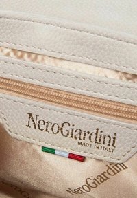 Interno in pelle bianca texture con etichetta dorata a rilievo "NeroGiardini Made in Italy" e un piccolo accento della bandiera italiana.