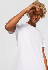 Weißes T-Shirt mit kurzen Ärmeln aus Baumwolle, ausgestattet mit einem Rundhalsausschnitt und einer lässigen Passform. Glatte Textur und einfaches Design ohne Muster.
