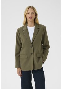 Olivovo zelený blazer s klopovými límci, jedným gombíkom na zapínanie a dvoma prednými vreckami; vyrobený z hladkej tkaniny, skombinovaný s bielym tričkom.