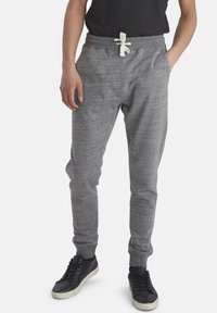 Pantalones de chándal grises hechos de tela suave, con cintura elástica, cierre de cordón, bolsillos laterales y piernas ajustadas.