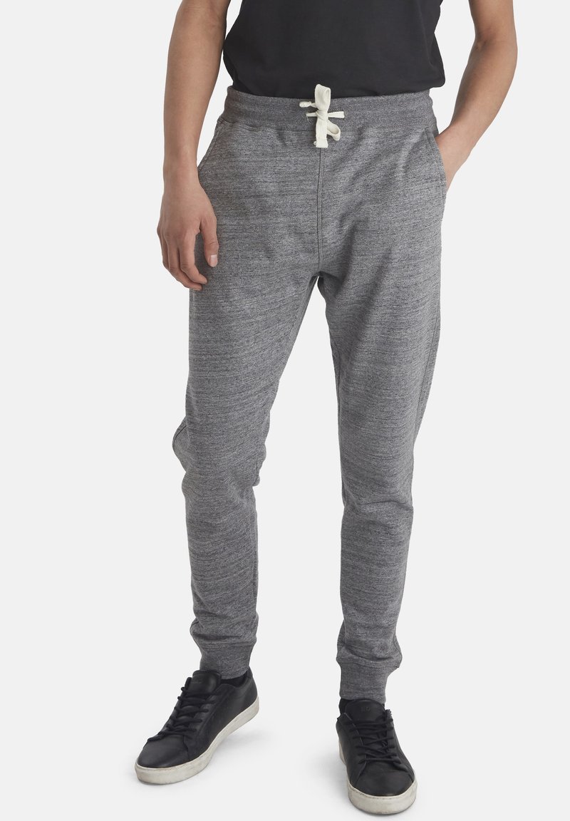 Pantalones de chándal grises hechos de tela suave, con cintura elástica, cierre de cordón, bolsillos laterales y piernas ajustadas.
