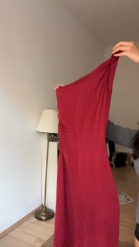 Rdeča, brezrokavna obleka iz gladkega blaga, z naborkom na strani. Prikazana, kako jo nekdo drži noter.