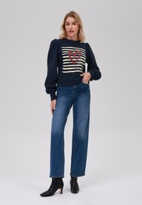 Sweatshirt bleu marine avec un design à rayures, un graphique de cœur rouge et des manches bouffantes, associé à un jean droit bleu clair et des bottines noires.