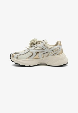 Chunky beige and white sneaker with metallic gold accents, thick cushioned sole, and lace-up closure, viewed from the outer side.