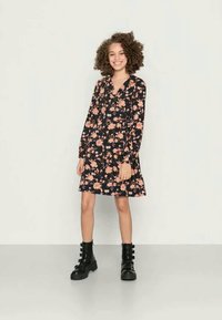 Vestido floral com fundo preto, apresentando flores rosa e brancas, mangas longas, decote em V e bainha desejada. Combinado com botas de combate pretas.