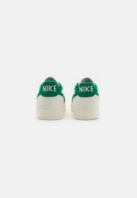 Valged Nike tossud roheliste aktsentidega. Lame tald, sile pind ja brändingu element taga. Minimalistlik disain klassikalise siluetiga.