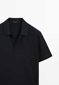 Polo nero in tessuto testurizzato, con maniche corte e colletto a polo. Presenta una placca discreta con un solo bottone.