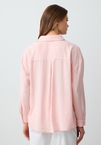 Lichtroze shirt, lange mouwen, knoopmanchetten, achterste plooidetail, ontspannen pasvorm, gladde textuur, kraagontwerp, geen zichtbare patronen.