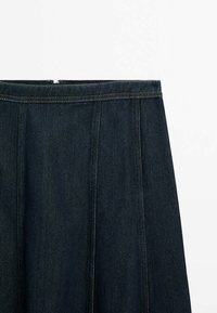 Jeanskjol i mörkblått med en strukturerad passform, prydd med veck, synliga sömmar och en dold dragkedja vid midjan.