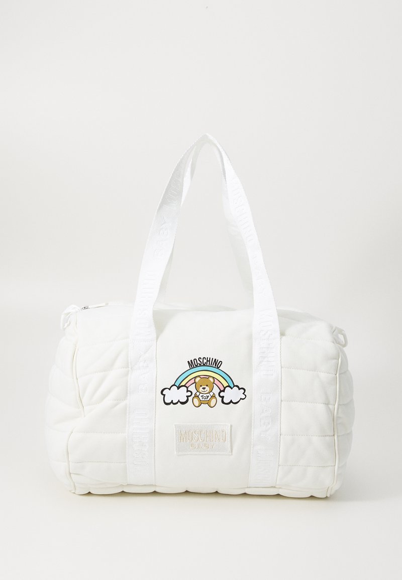 White quilted duffle bag with fabric handles, featuring a bear and rainbow design, branded patch, and glossy accents. Zipper closure.