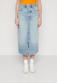 Světle modrá džínová midi sukně s předním rozparkem, dvěma předními kapsami a poutky na opasek, v kombinaci s bílými teniskami a ponožkami do kotníků.