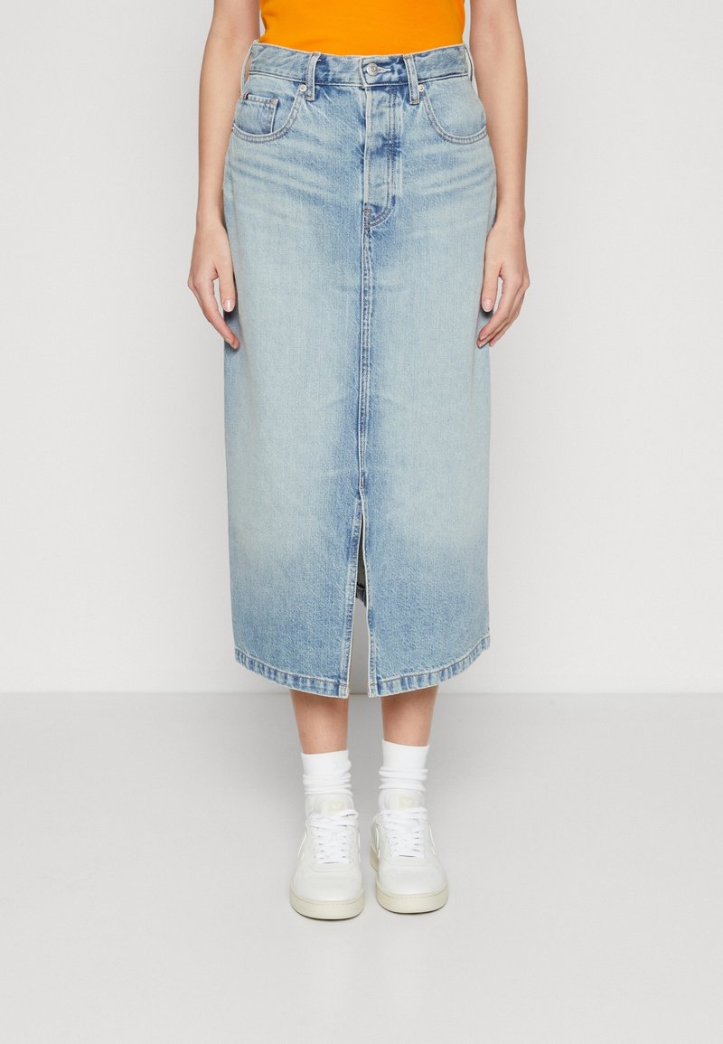 Světle modrá džínová midi sukně s předním rozparkem, dvěma předními kapsami a poutky na opasek, v kombinaci s bílými teniskami a ponožkami do kotníků.