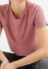 Růžové texturované tričko s krátkým rukávem a kulatým výstřihem; viditelný vzor dodává jemný detail; hladká tkanina s mírným leskem.