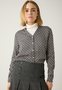 Blouse met knopen in zwart-wit geometrisch patroon, lange mouwen met knoopmanchetten, gecombineerd met een hooggepolsterde grijze geruite rok met knopen.