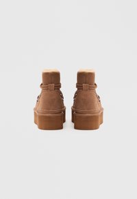 Bruine suede enkellaarzen met een pluizige voering, ronde neus, vetersluiting en dikke plateauzool. Achteraanzicht toont een gladde textuur en stikdetails.