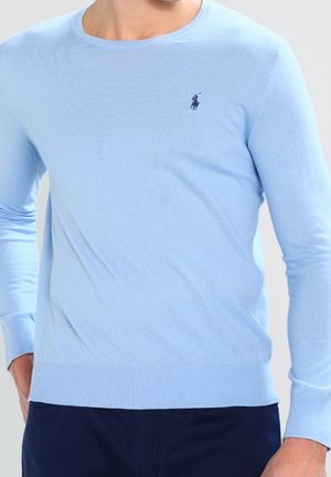 Light blue long-sleeve sweater with a small dark blue embroidered logo on the left chest, paired with dark navy pants.