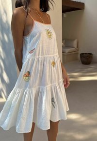 Biele bavlnené šaty s tenkými ramienkami, viacvrstvovým strihom, vyšívanými kvetinovými a ovocnými motívmi a voľným strihom.