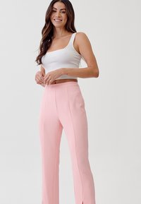 Witte geribbelde crop top en roze high-waisted broek met splitten aan de zijkant. De outfit heeft een getailleerd ontwerp en een soepele stoftextuur.