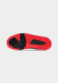 Μαύρη και κόκκινη σόλα αθλητικού παπουτσιού με υφασμένα μοτίβα από καουτσούκ, που διαθέτει εμφανές λογότυπο και χαρακτηριστικό σχέδιο πρόσφυσης.