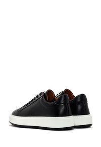 Black leather sneakers with a smooth texture, featuring a white rubber sole, rounded shape, and flat laces. Interior lined with brown material.
